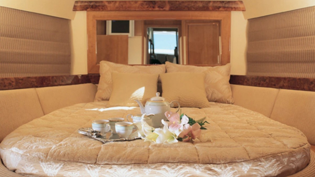 Cozy boat cabin with a round bed, pillows, a tea set on a tray, and flowers.