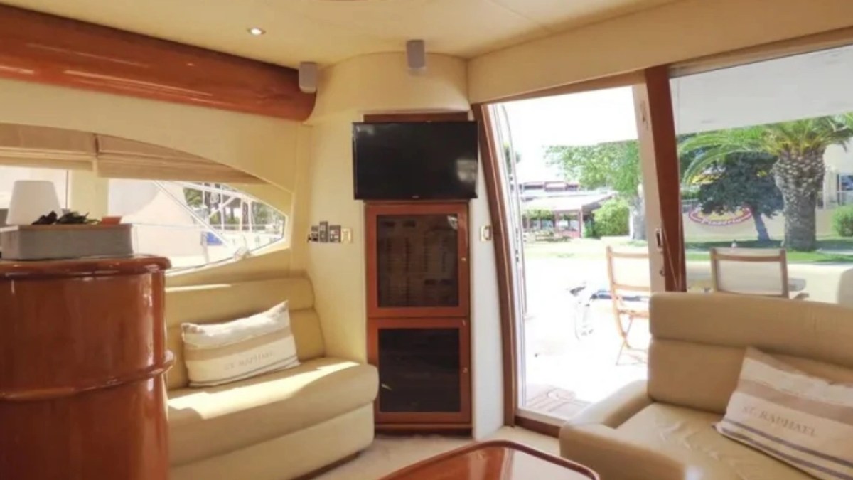 Interior of a yacht with beige sofas, wood paneling, TV, and view of outdoors through sliding glass door.