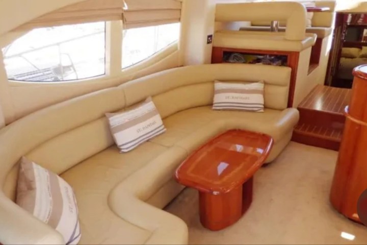 Interior of a yacht with a curved beige sofa and a wooden coffee table.