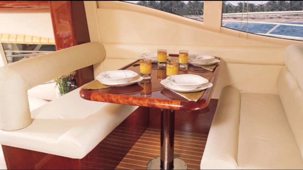 Luxurious yacht dining area with wood table set with juice and plates, cream seats, and ocean view.