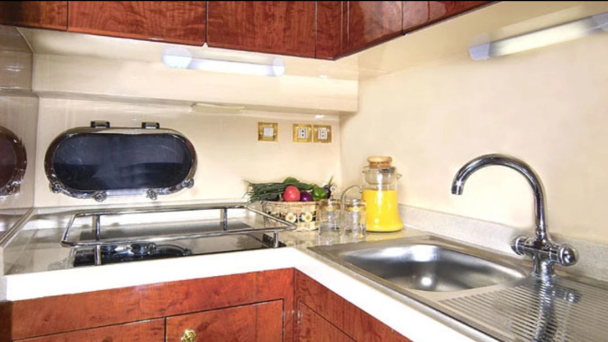 Small kitchen with sink, stovetop, porthole window, and fruit on counter.