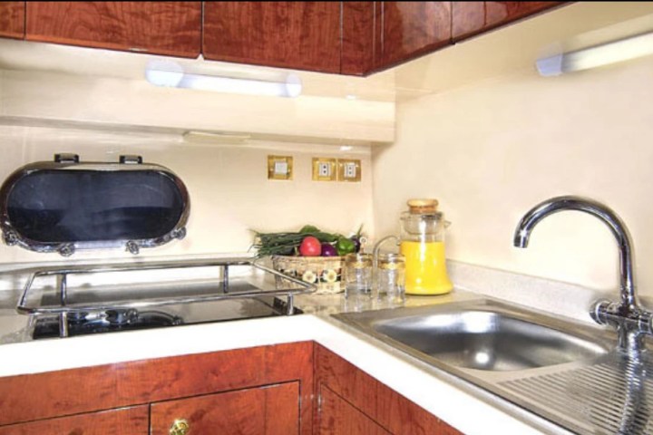 Small kitchen with sink, stovetop, porthole window, and fruit on counter.