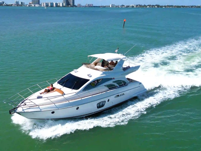 Luxury yacht cruising on a clear blue ocean near a city skyline.