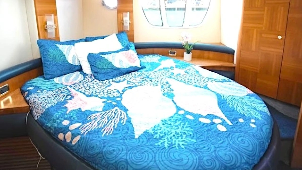 Boat cabin with a bed, blue seashell bedding, small window, and wooden decor.
