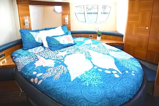 Boat cabin with a bed, blue seashell bedding, small window, and wooden decor.