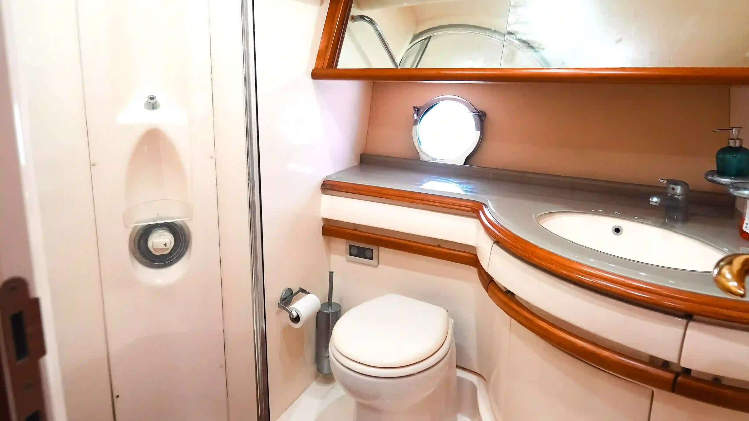 Compact yacht bathroom with toilet, sink, shower, and mirror.