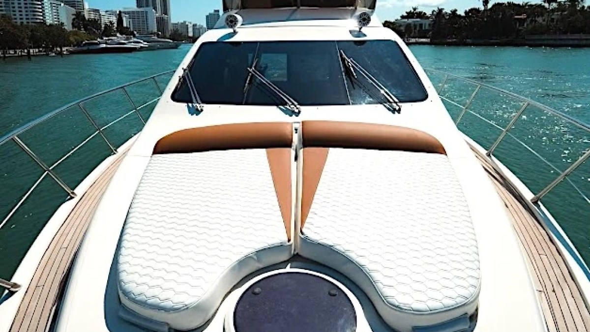 View from yacht deck with sun loungers, sea, city skyline, and palm trees in the background.