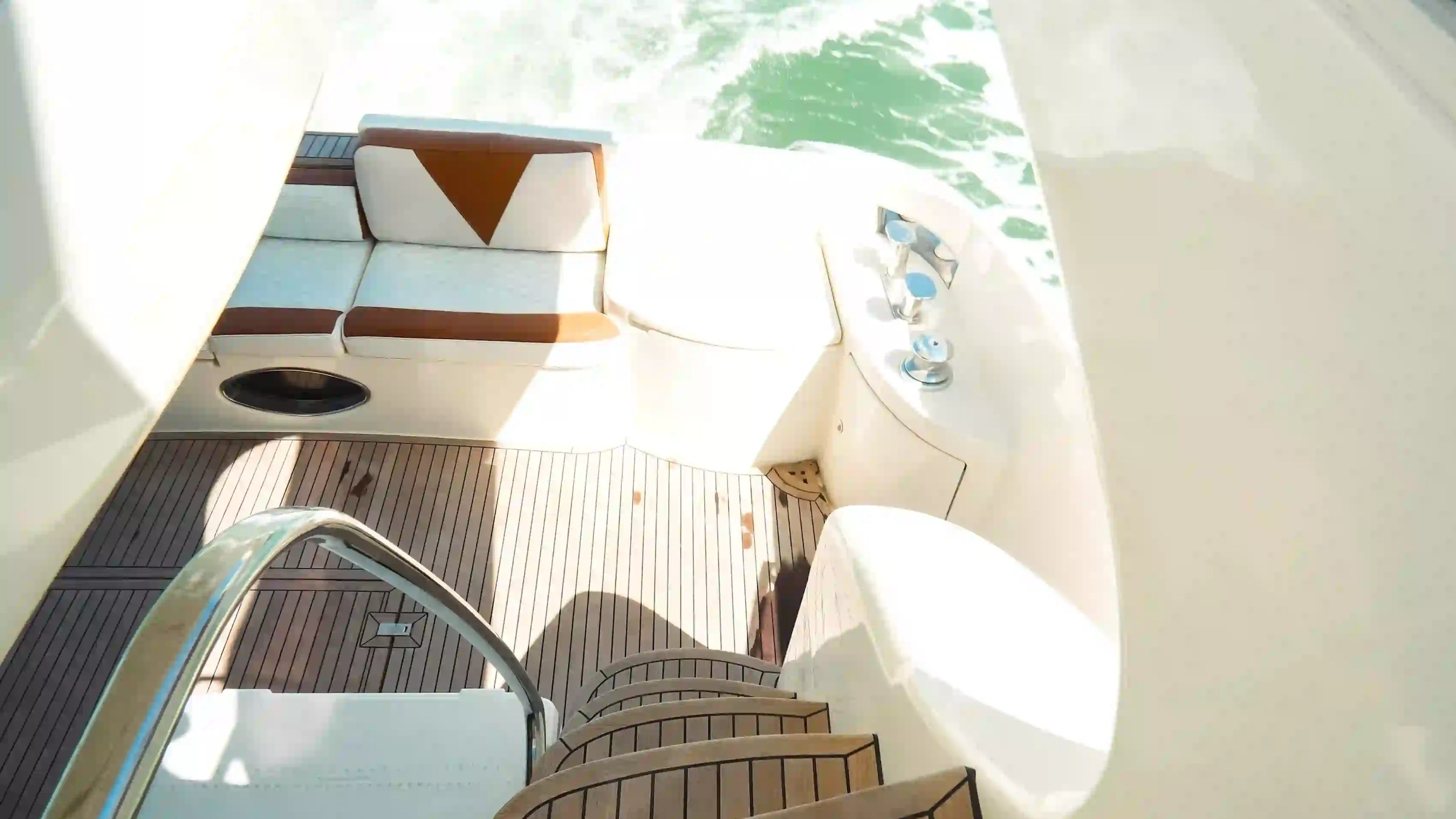 View of a yacht's deck with wooden steps, seating, and a water view.