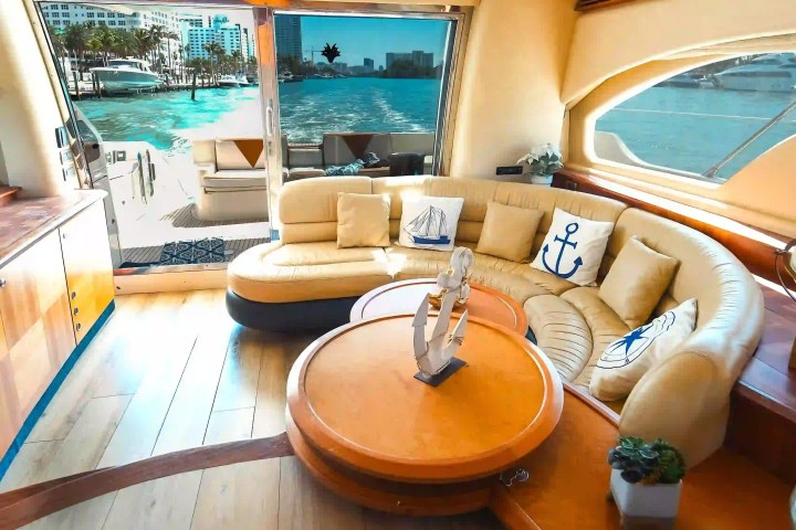 Luxurious yacht interior with beige seating, round table, and ocean view through large sliding glass doors.