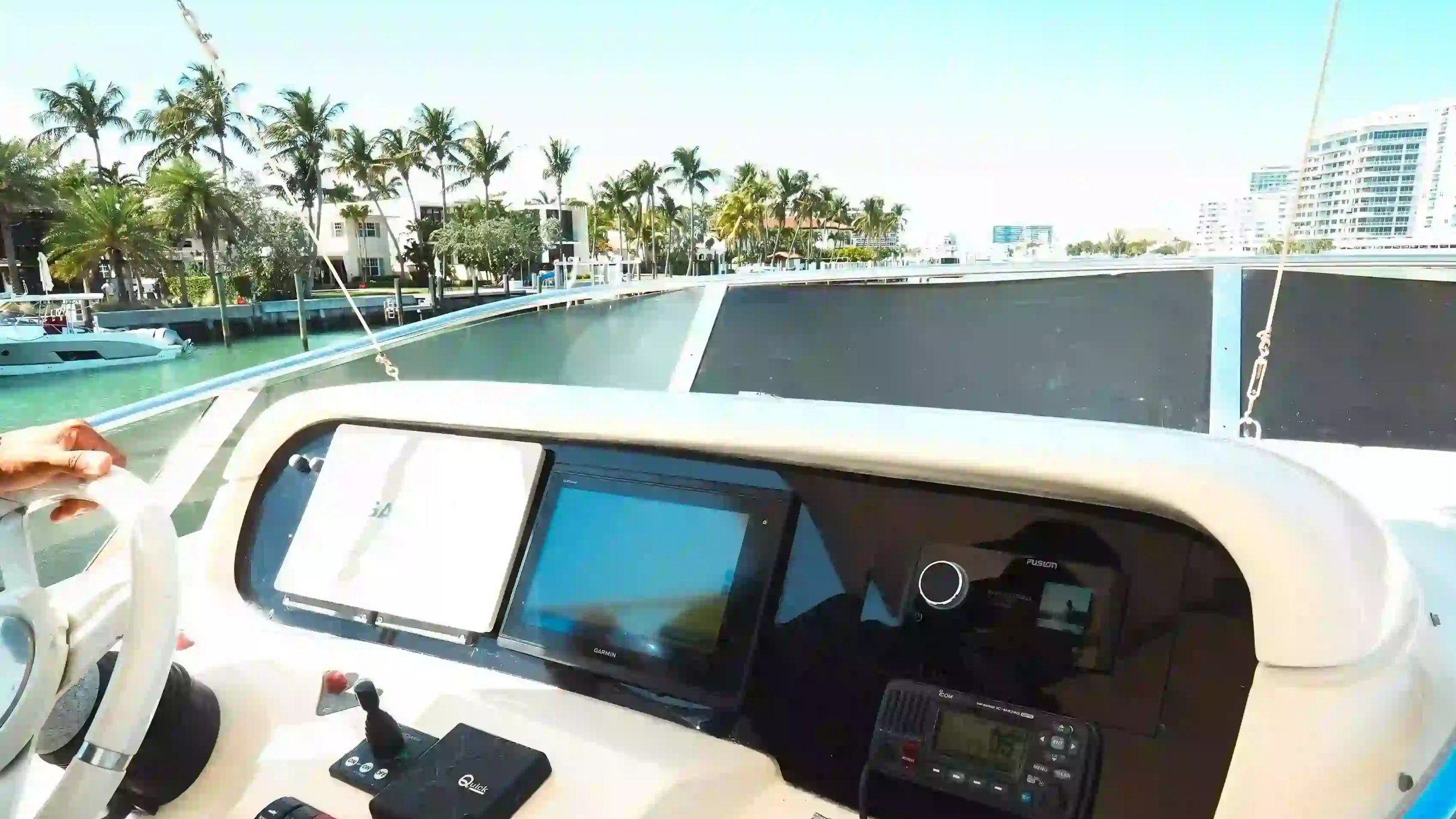 Boat control panel with screens and controls, overlooking palm trees and waterway.