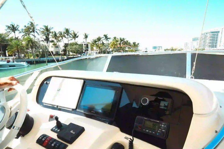 Boat control panel with screens and controls, overlooking palm trees and waterway.