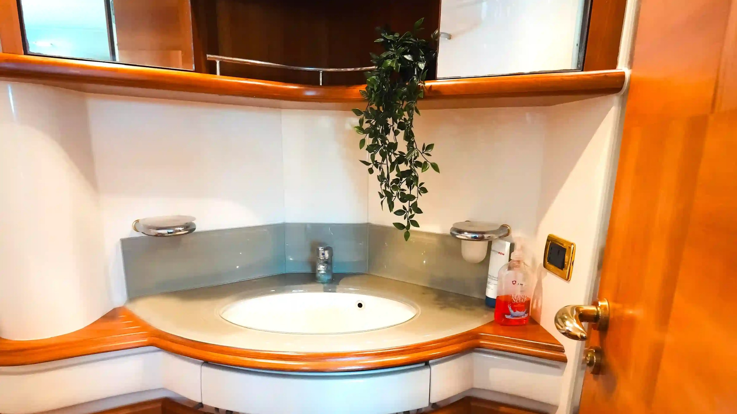 Compact bathroom with round sink, mirrors, and plant on shelf.