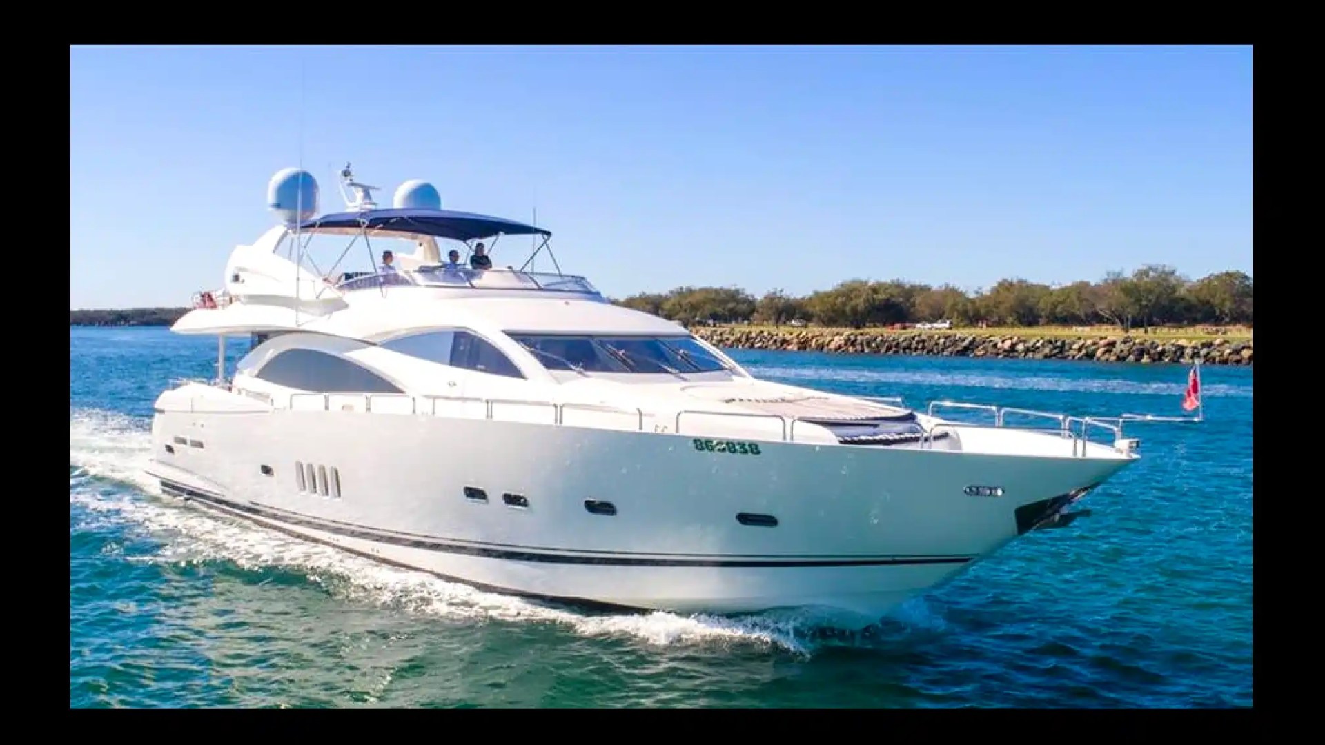 White luxury yacht cruising on blue water with trees in the background.