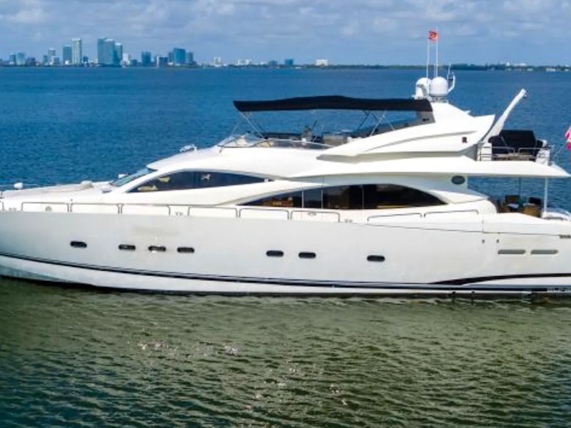 Large white yacht on water with city skyline in the background.