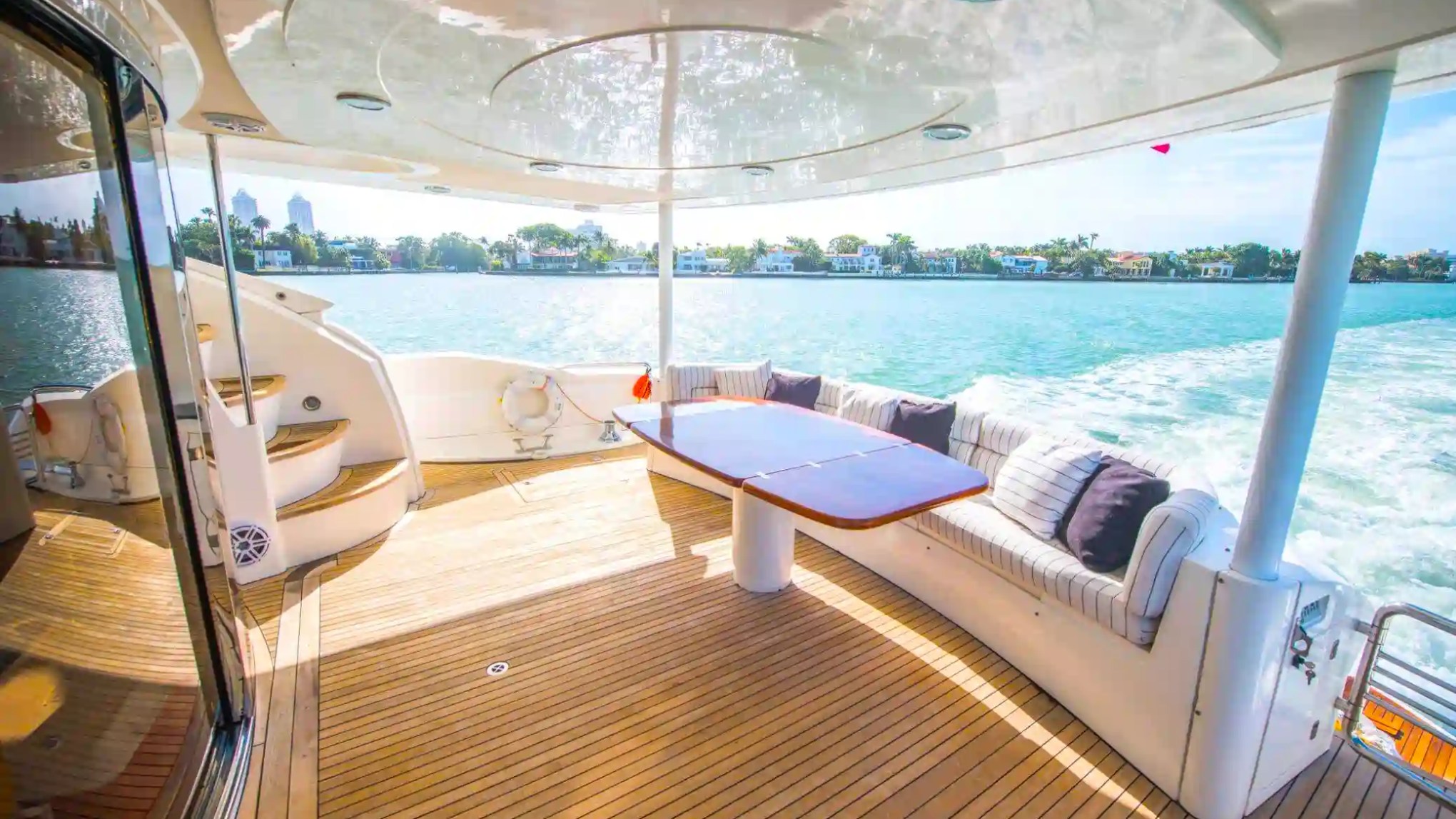 Yacht deck with curved sofa, table, and sea view under a covered canopy.