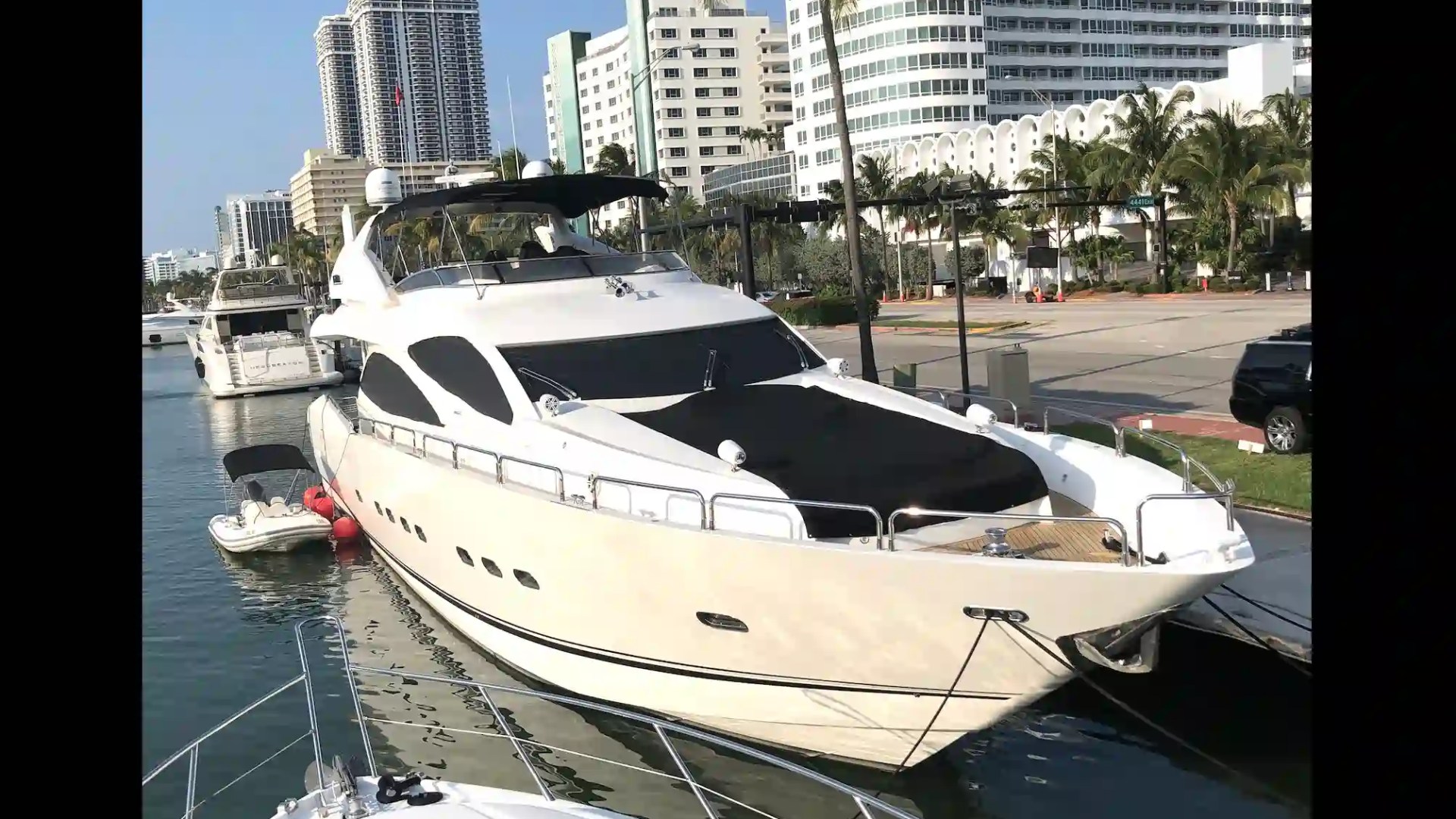 Luxury yacht docked in marina with high-rise buildings and palm trees in the background.