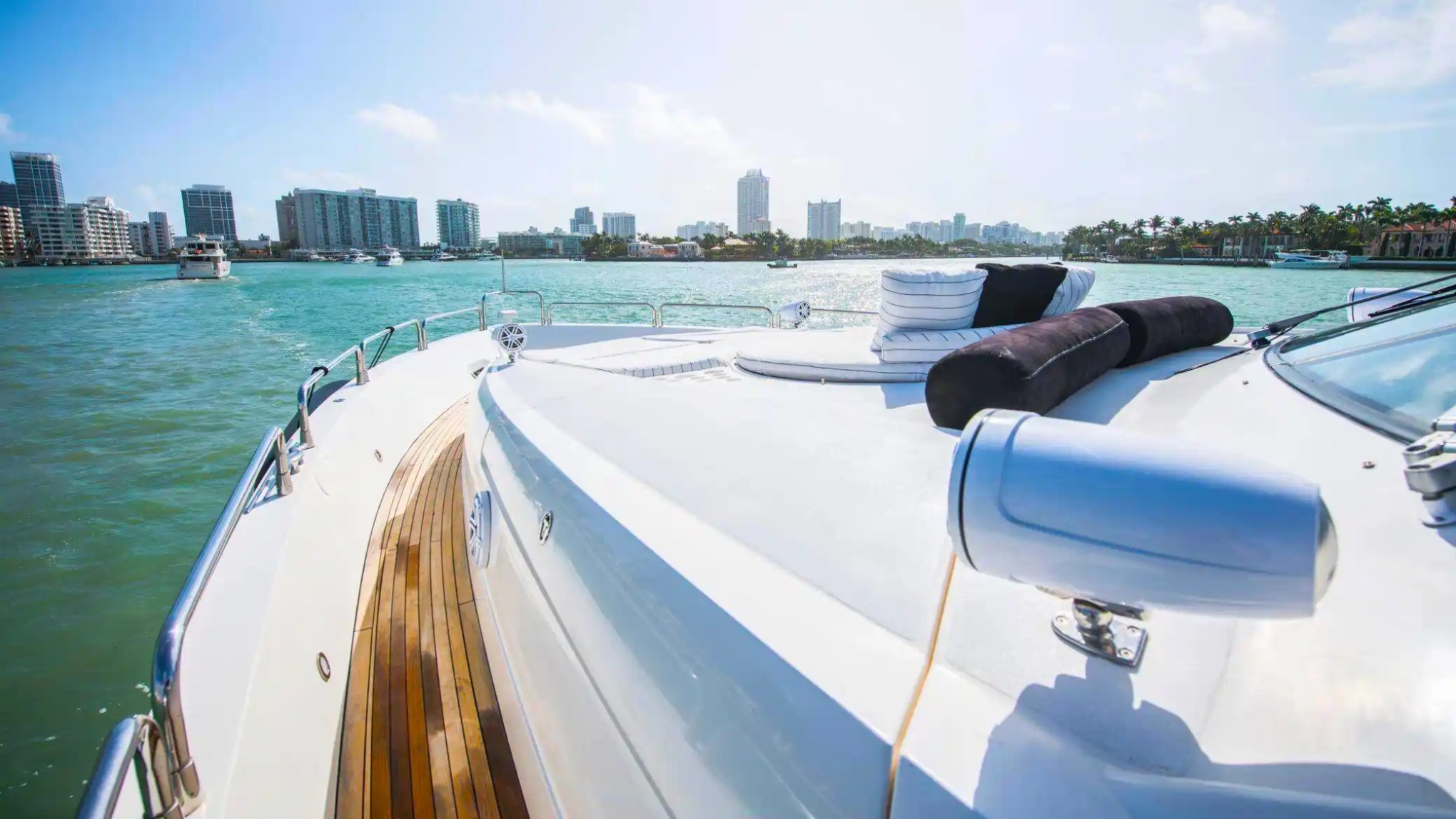 Yacht deck with cushions facing a city skyline across calm water on a sunny day.