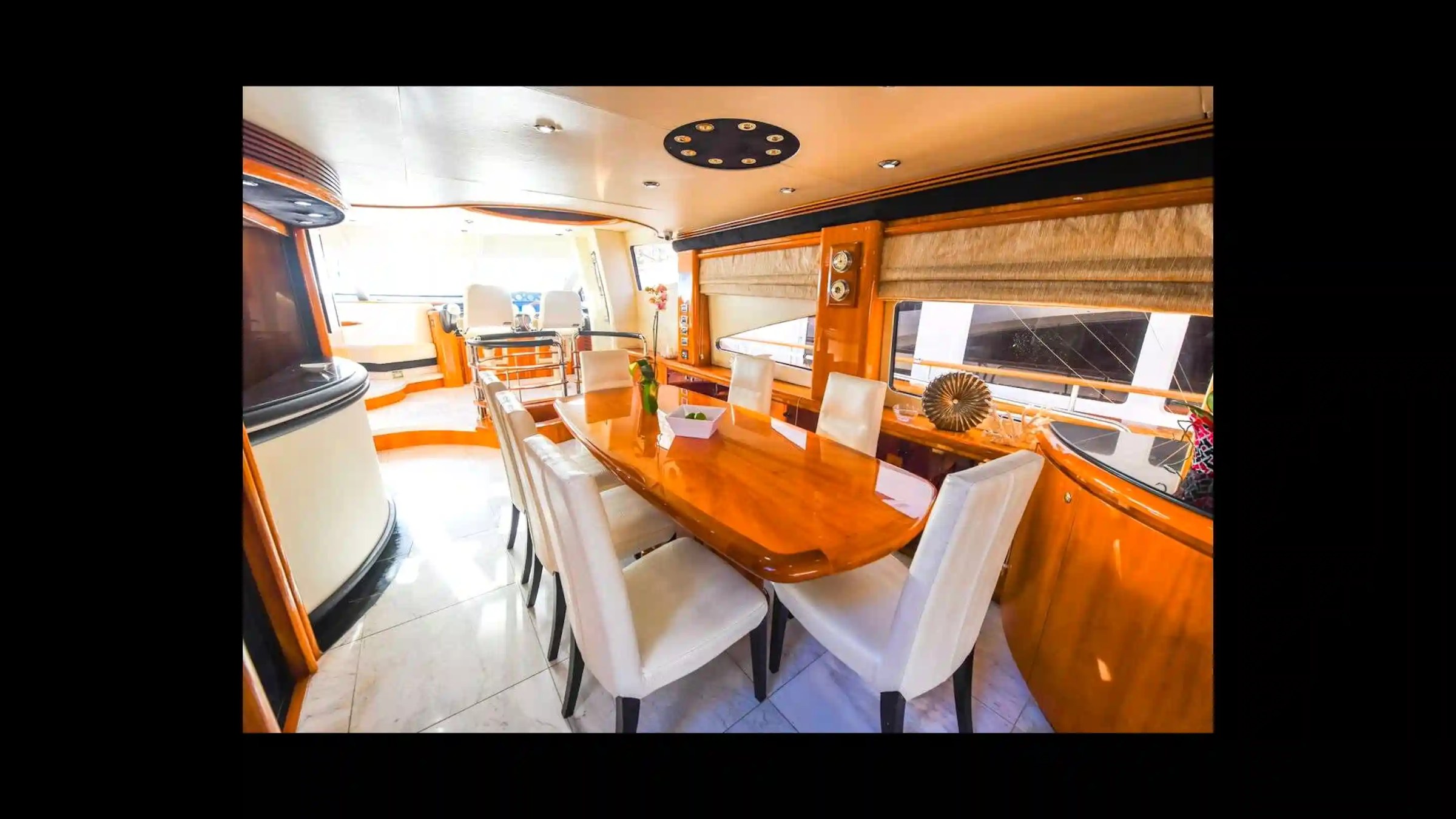 Luxurious yacht dining area with wood table and white chairs, sunny view.