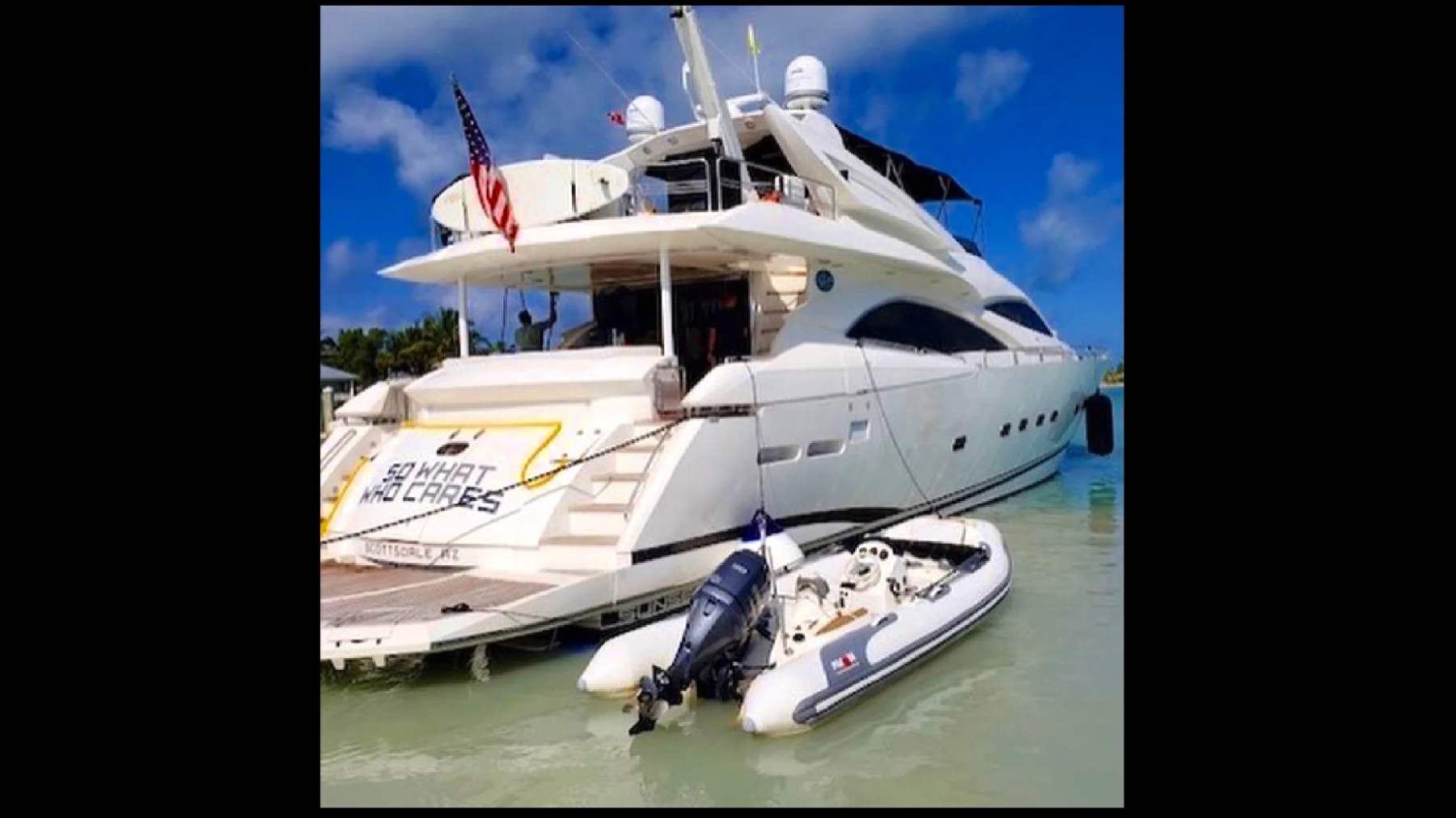 Large white yacht with an American flag and a small dinghy attached, floating in calm water.
