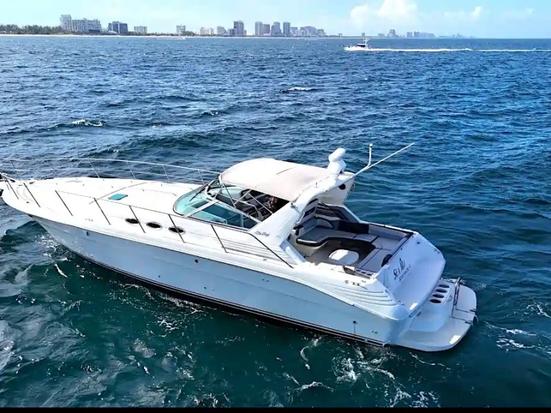 White yacht on open ocean with distant city skyline.