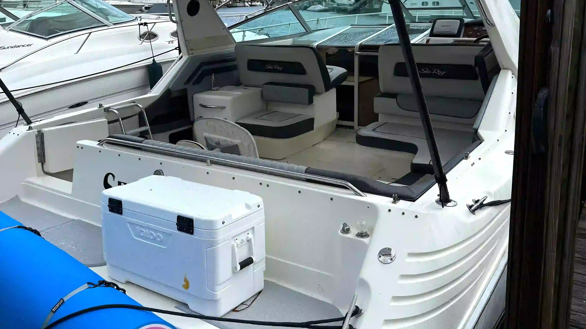 Rear view of a docked white motorboat with seating and a cooler on deck.