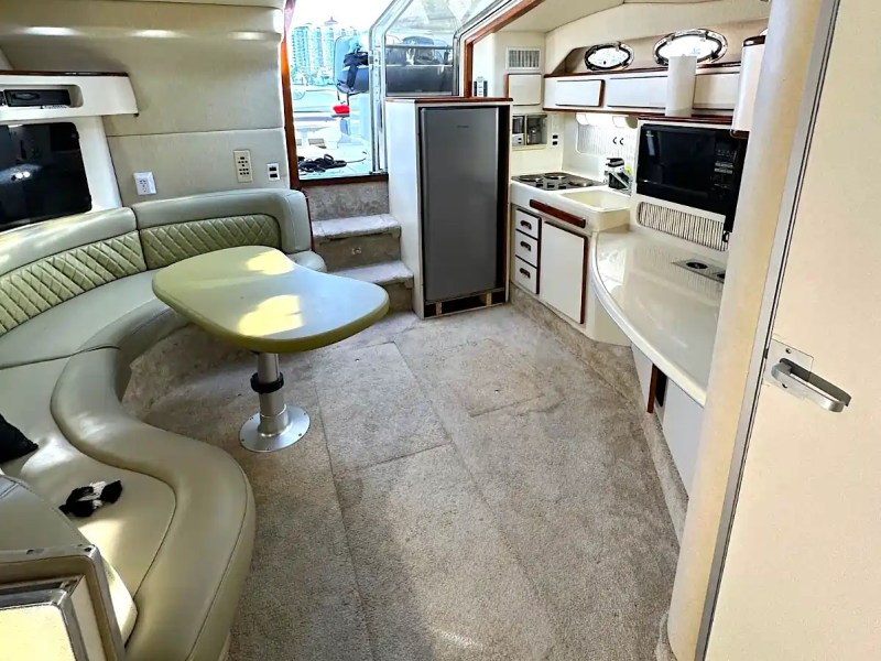 Interior of a boat with seating, table, kitchenette, and stairs.