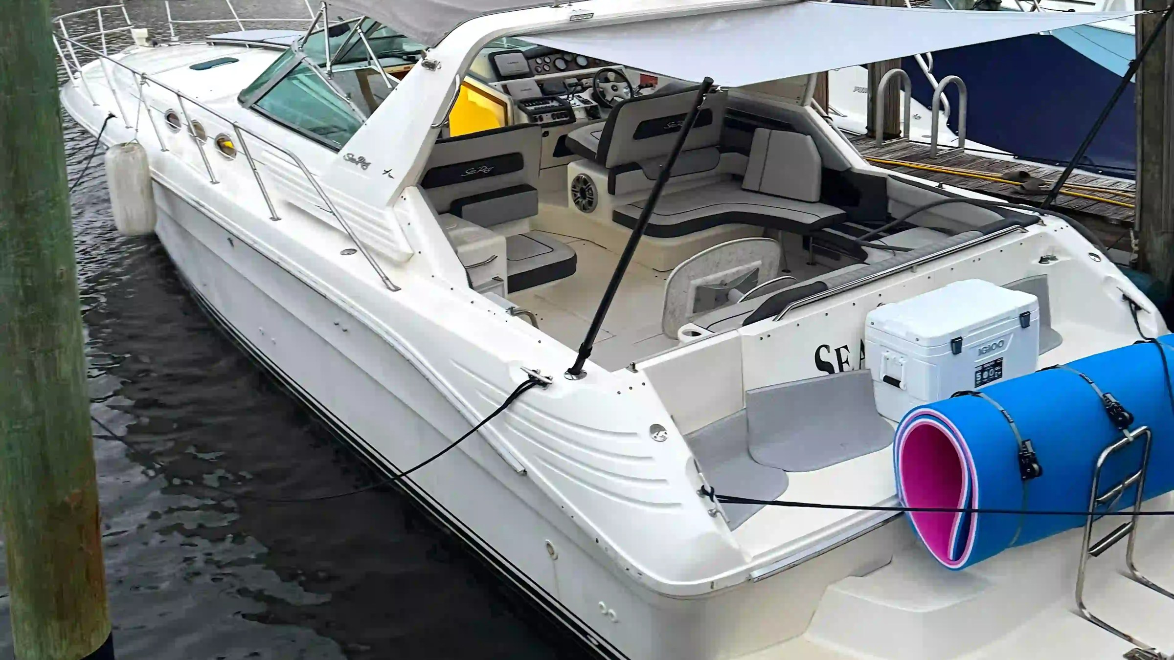 White motorboat docked, with canopy and American flag, cooler and floatation device on deck.