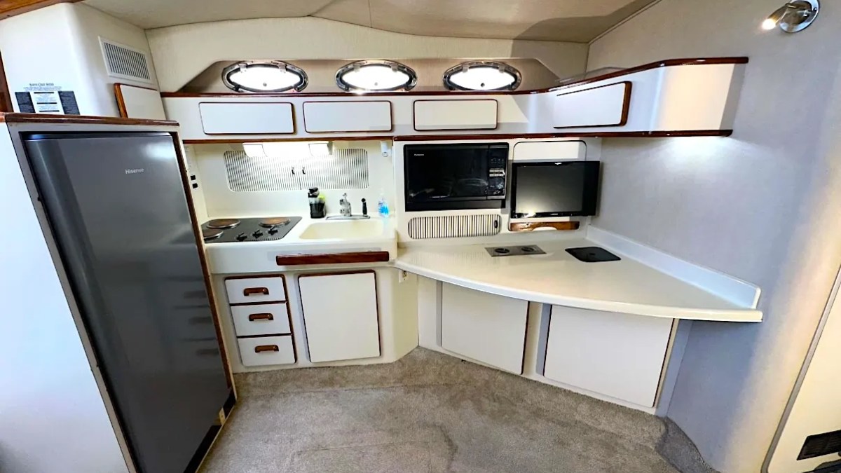 Boat kitchen with stove, fridge, and cabinets in compact white interior.