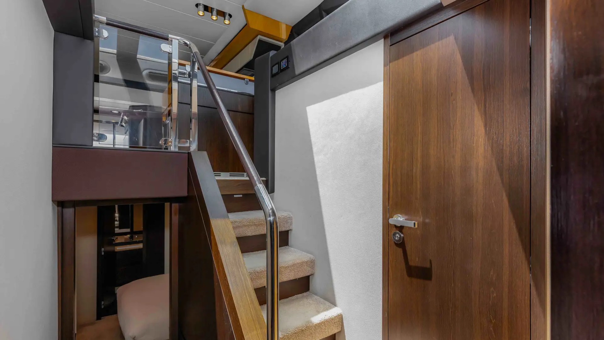 Modern yacht interior with stairs, wooden door, and glass railing.