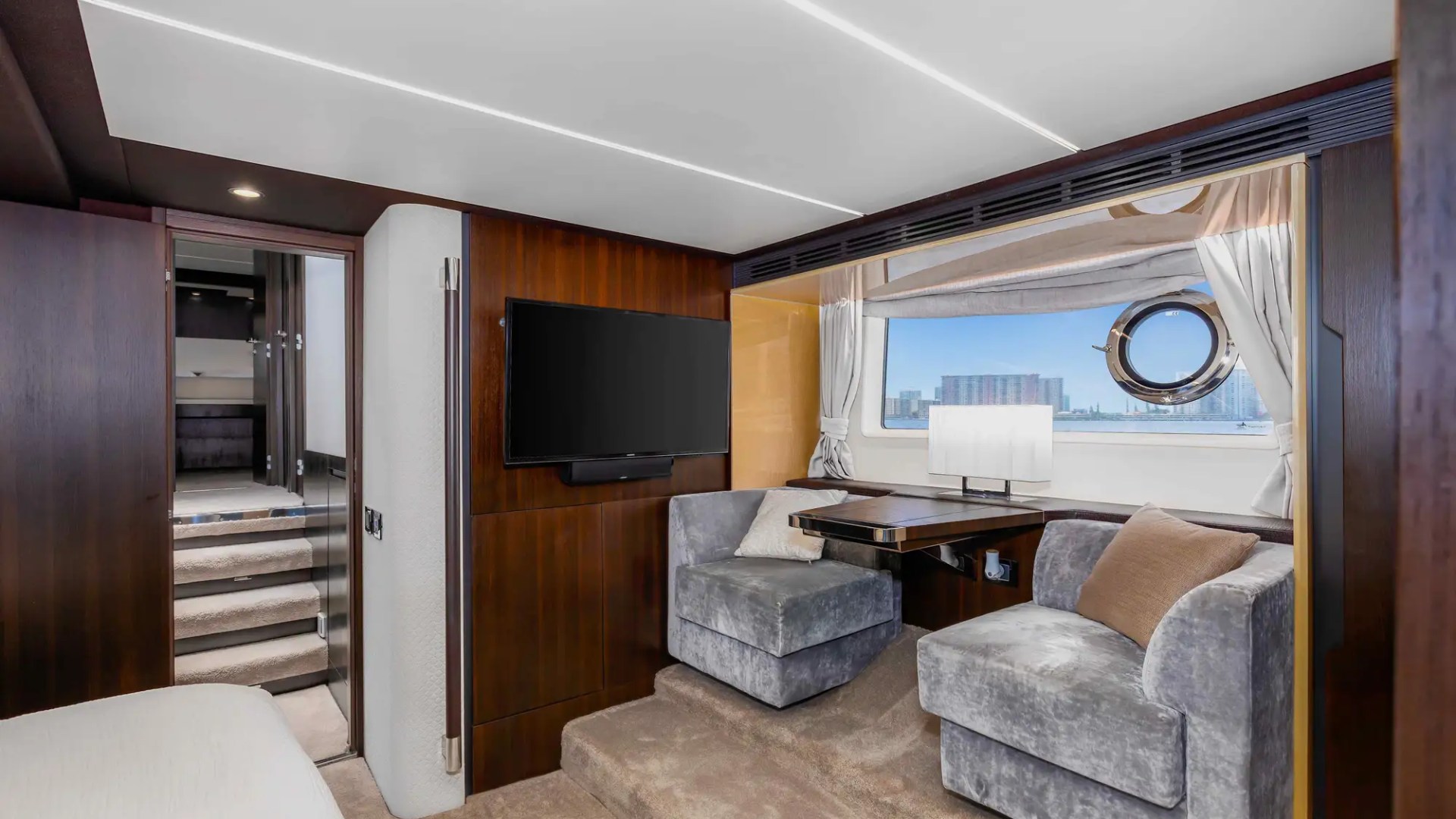 Luxurious yacht interior with armchairs, TV, window view of city skyline.