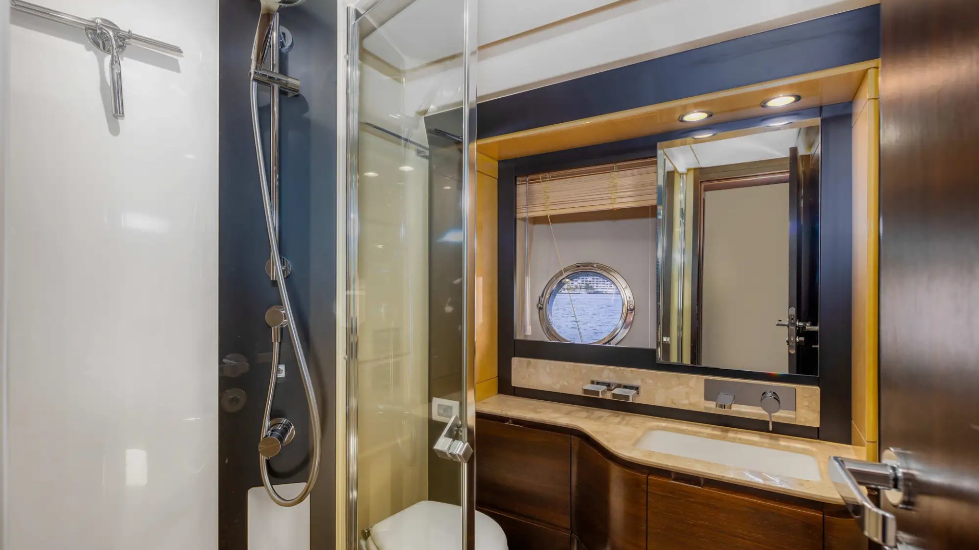 Modern yacht bathroom with glass shower, vanity, and porthole window.