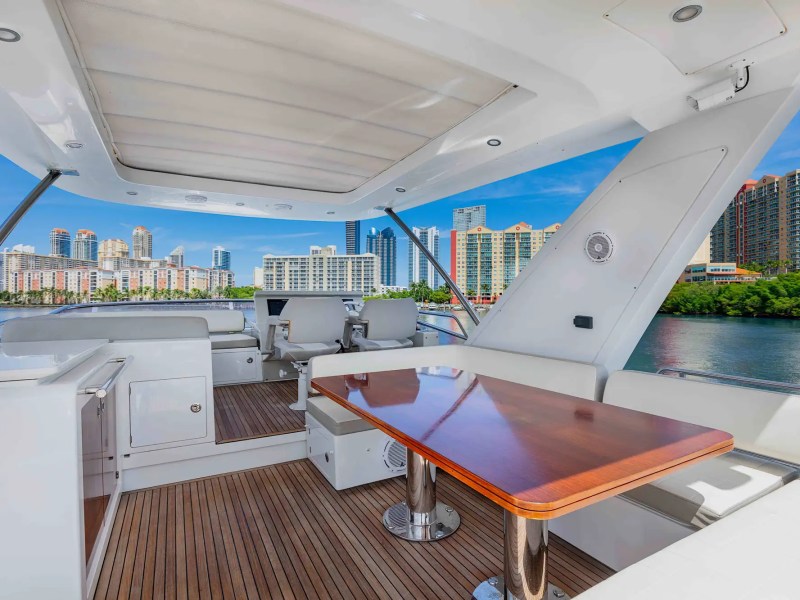 Luxury yacht deck with wooden table, seating, and city skyline view.