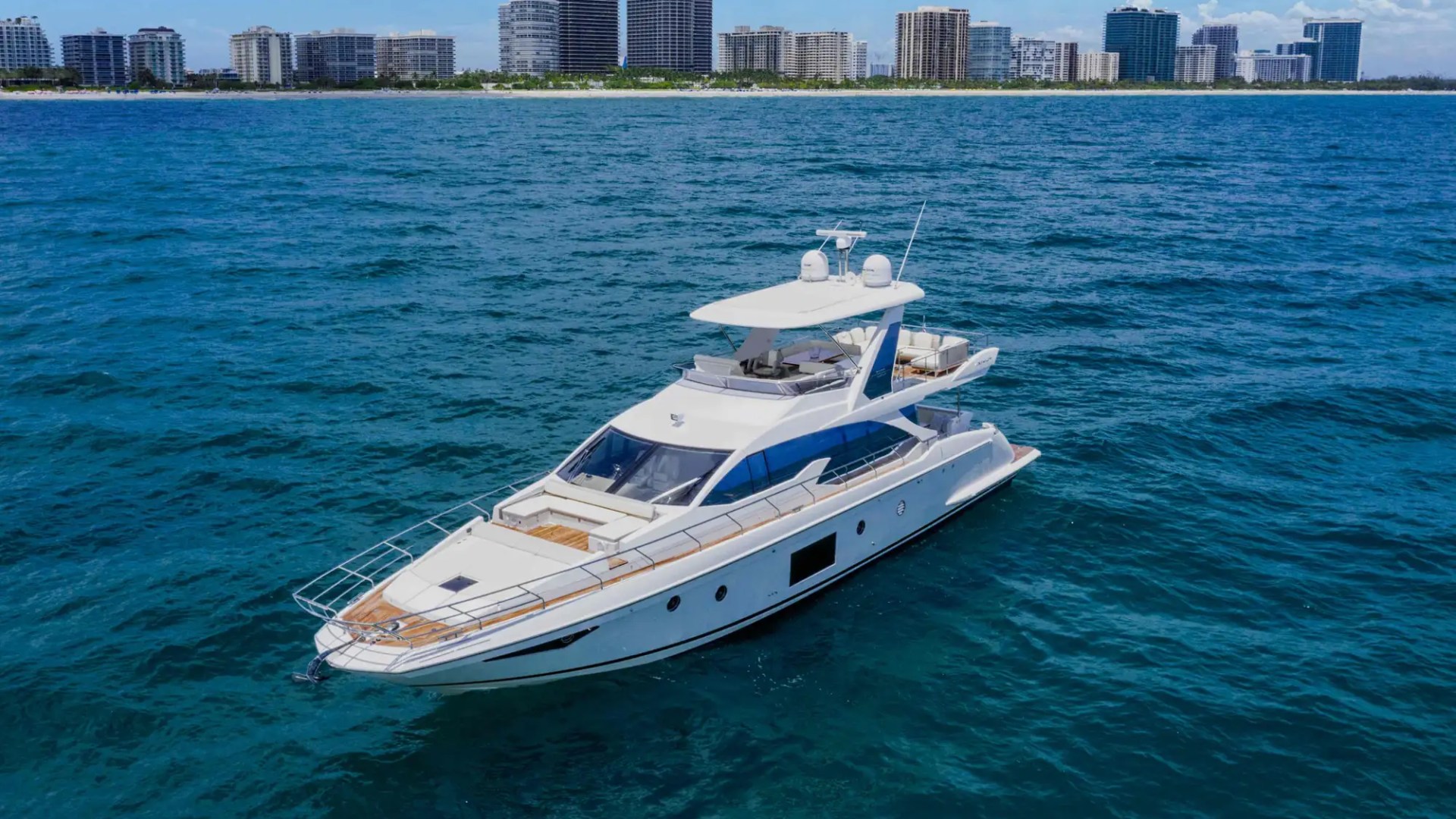 Luxury yacht sailing on blue ocean near a city skyline.