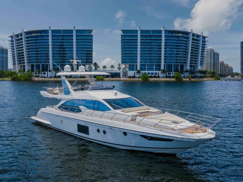 White yacht on water with modern high-rise buildings in the background.