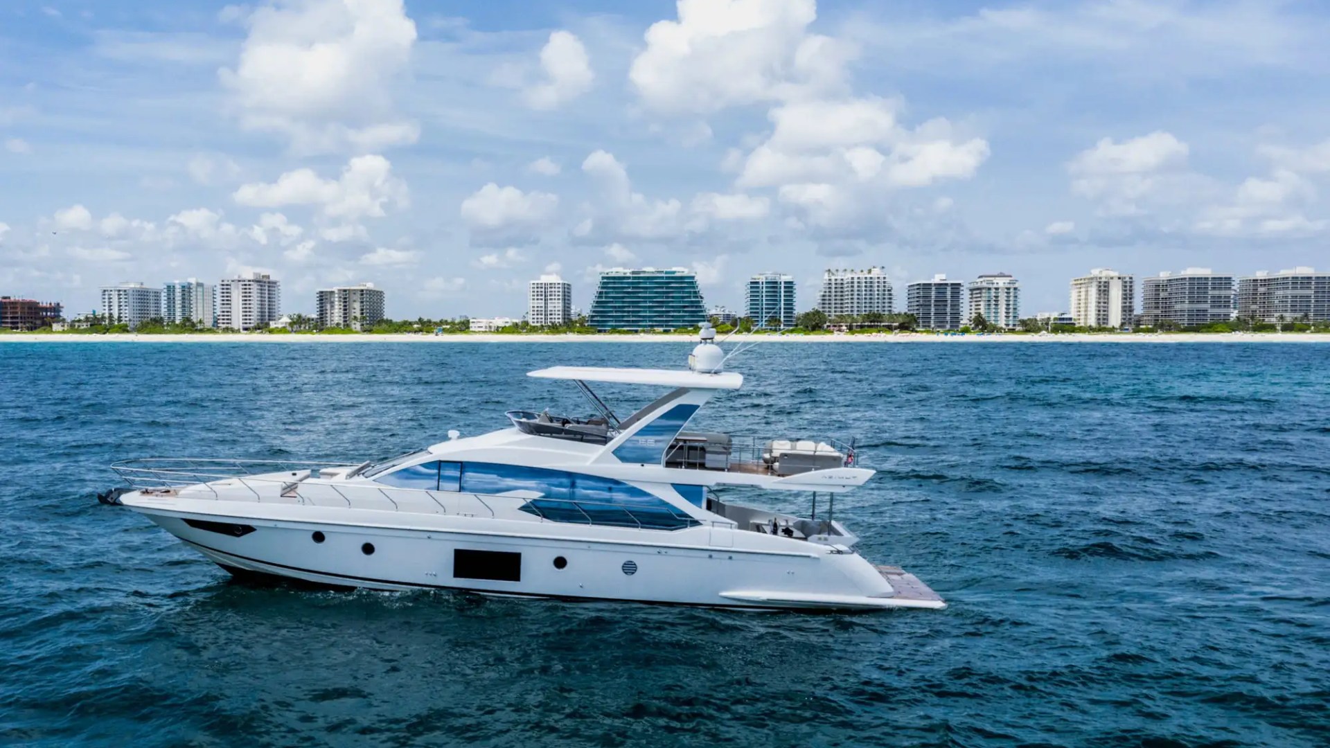 Luxury yacht cruising on blue ocean with city skyline in the background.