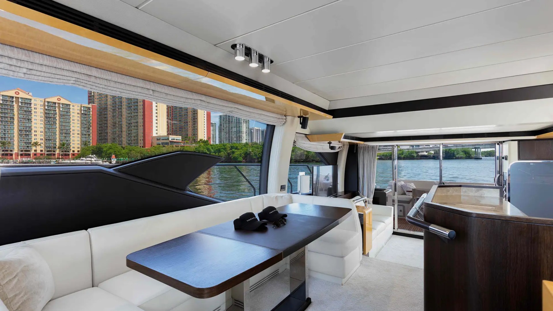 Luxurious yacht interior with white seating, table, and river view through large windows.