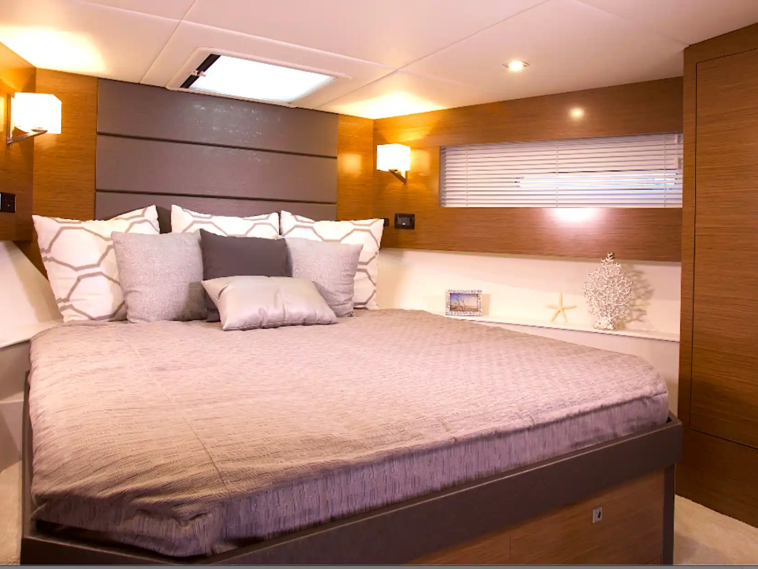 Cozy boat bedroom with a double bed, pillows, wooden walls, and soft lighting.