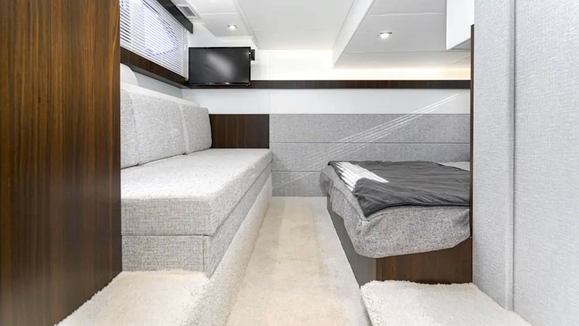 Modern yacht cabin with sofa, bed, and TV.