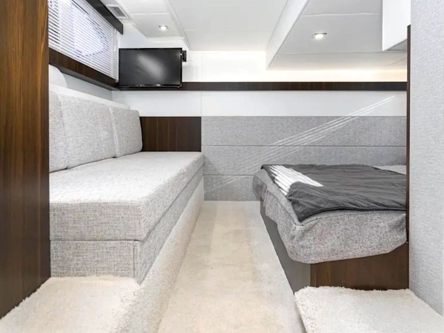 Modern yacht cabin with sofa, bed, and TV.