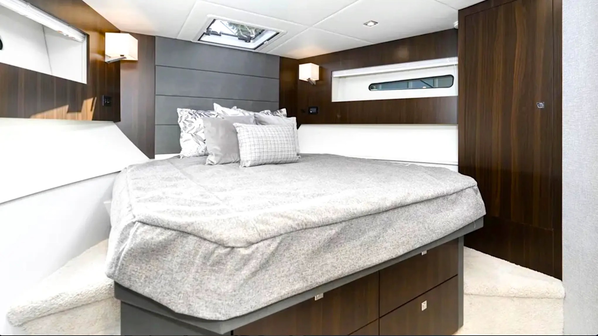 Interior of a bedroom with a gray bed, wood paneling, and wall lamps.