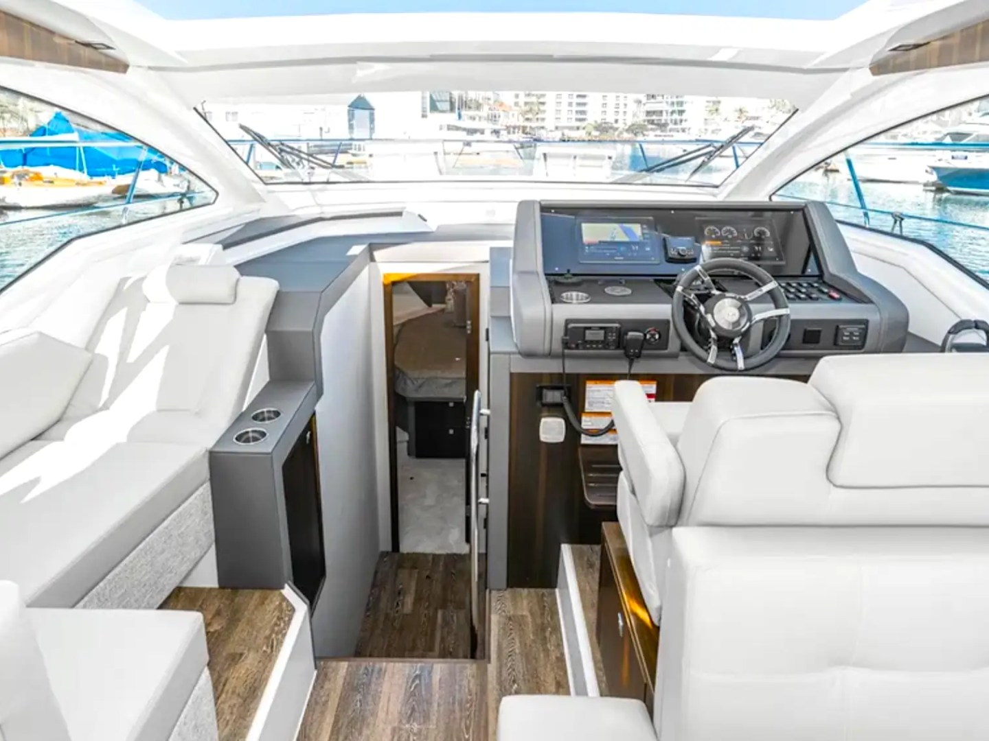 Luxurious yacht cockpit with steering wheel, screens, and plush white seating overlooking marina.