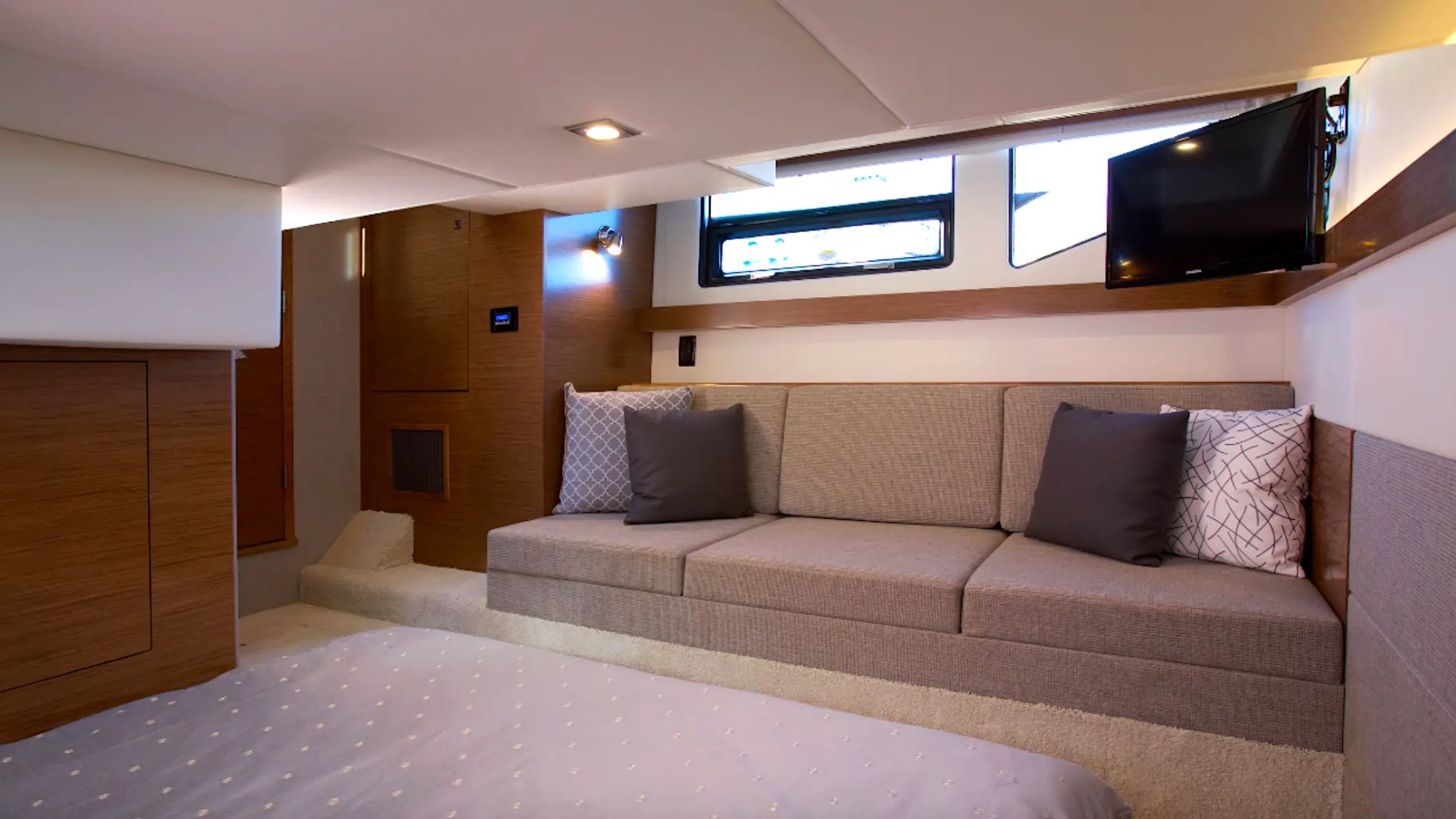 Interior of a yacht cabin with a sofa, bed, TV, and window.