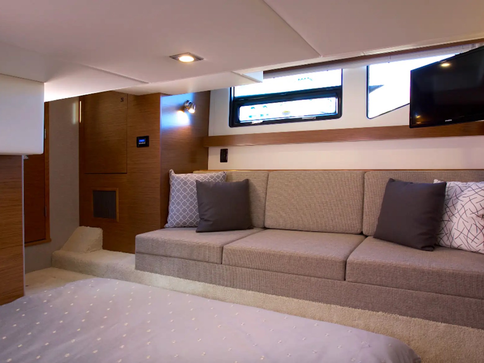 Interior of a yacht cabin with a sofa, bed, TV, and window.