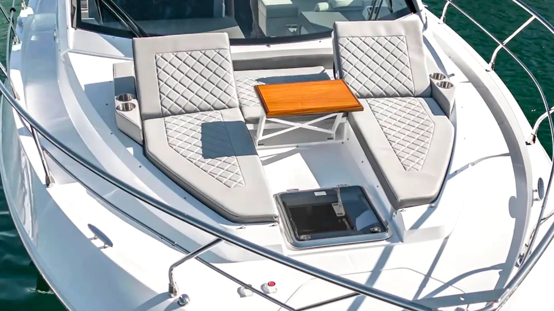 Sun deck of a yacht with two cushioned lounge chairs and a small wooden table.