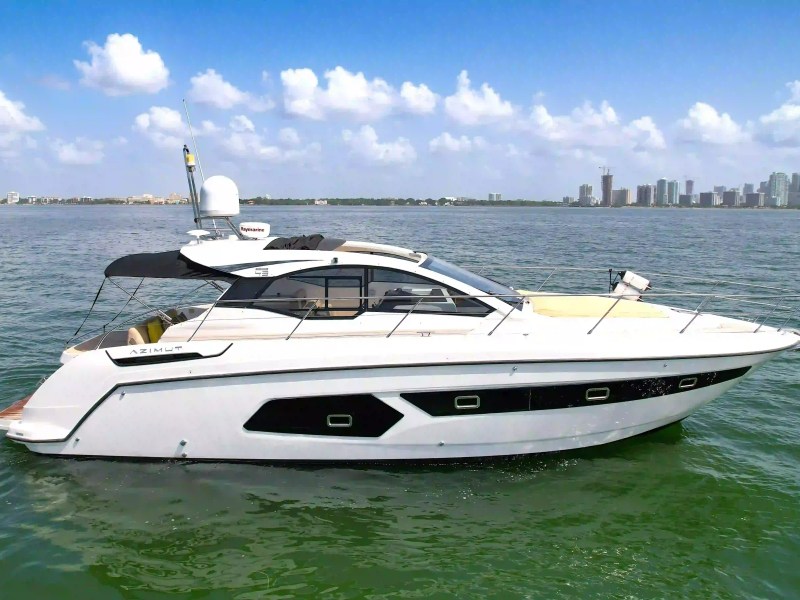 Luxury yacht on calm water with city skyline in background.