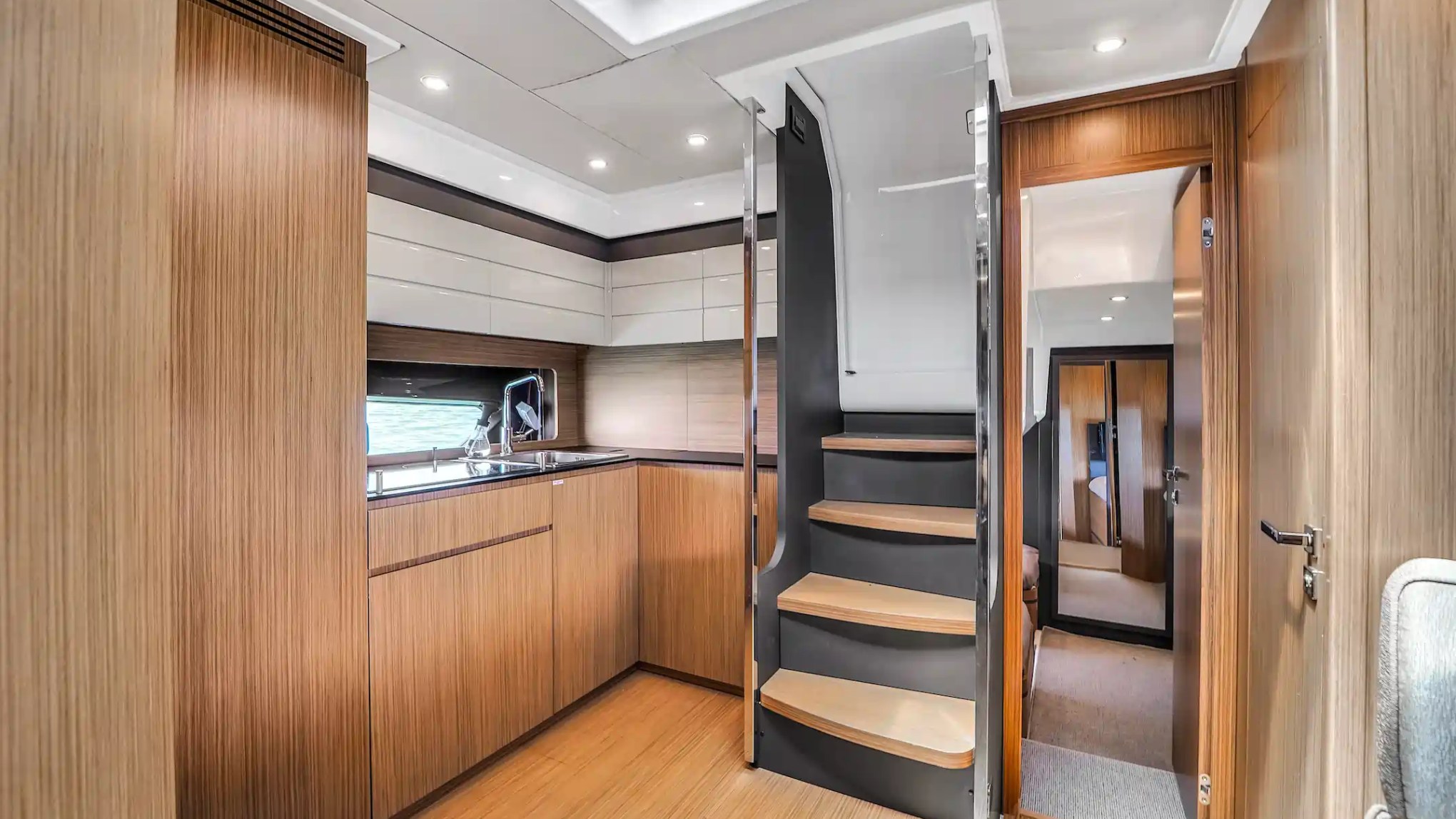 Modern boat interior with wooden paneling, stairs, and kitchenette.
