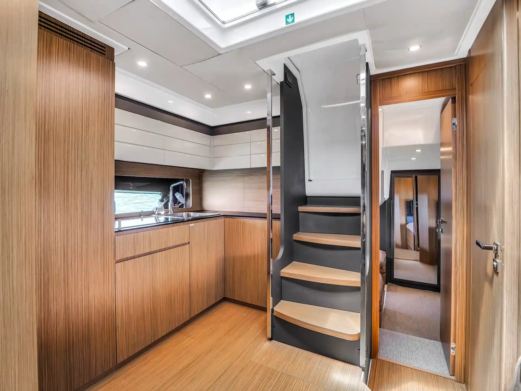 Modern boat interior with wooden paneling, stairs, and kitchenette.