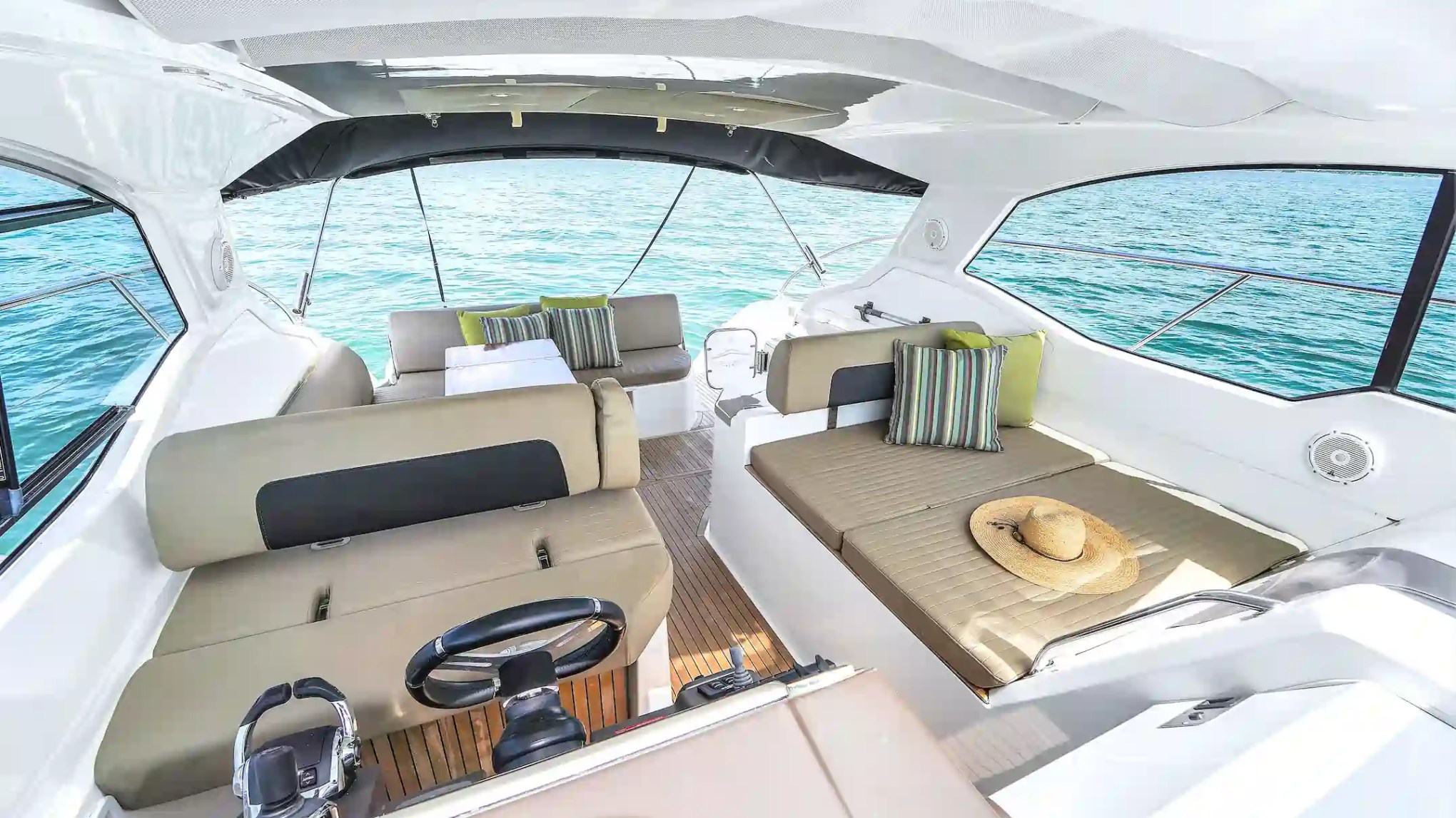 Interior view of a boat cabin with cushioned seats and ocean visible through large windows.