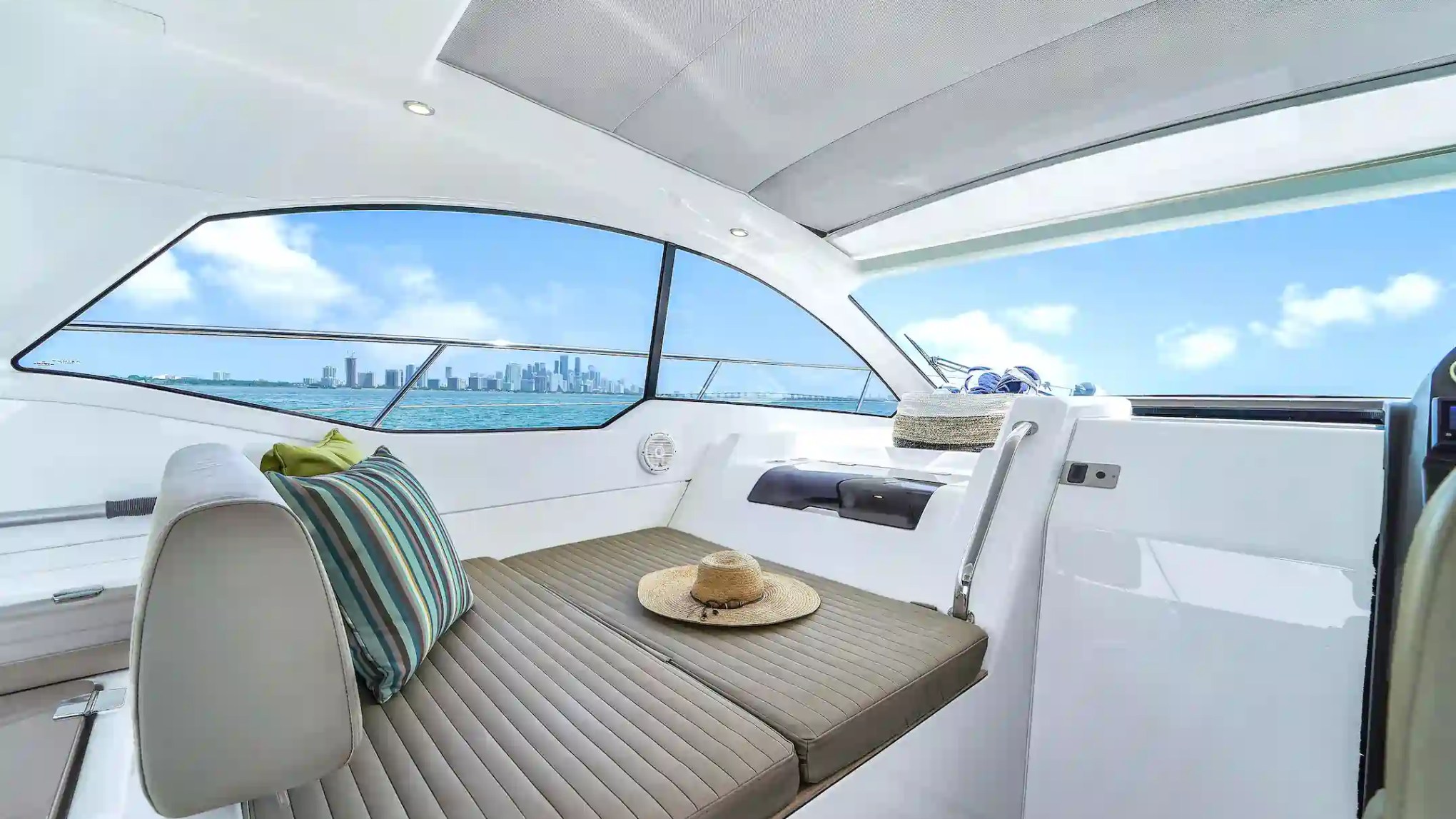Interior of a boat with seating, a hat, and a view of city skyline through windows.