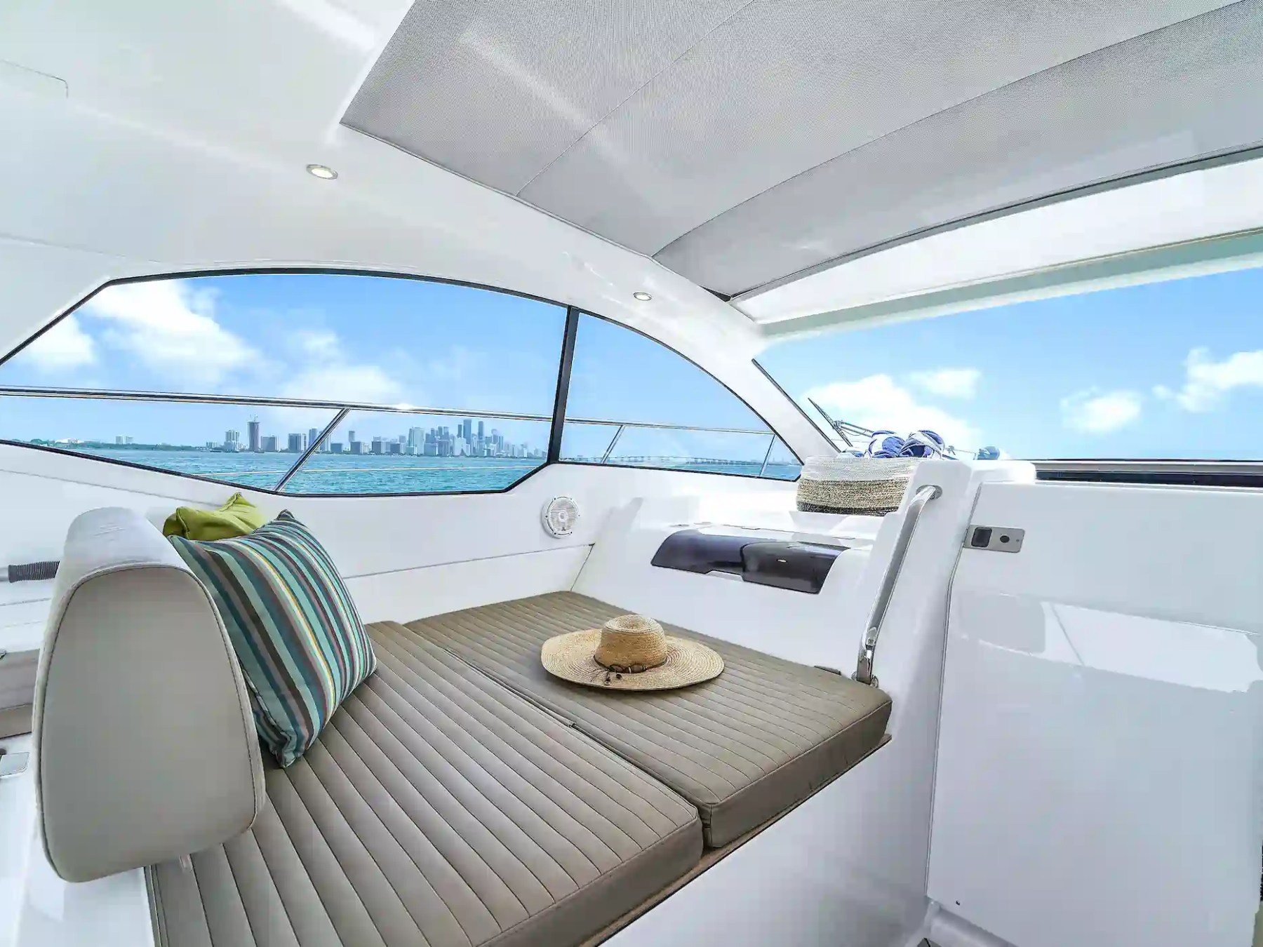 Interior of a boat with seating, a hat, and a view of city skyline through windows.